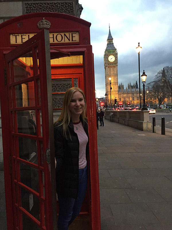 Claire Anderson in an old telephone booth in London that still works for emergency numbers. Big Ben and Westminster Abbey are in the distance.