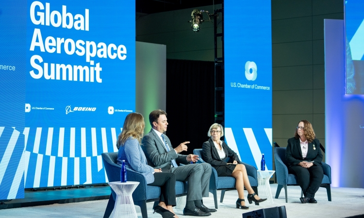 Four people sitting in chairs in front of a large sign that says Global Aerospace Summit