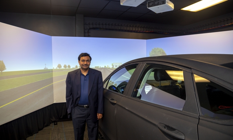 Srinivas Peeta stands next to the driving simulator in his lab