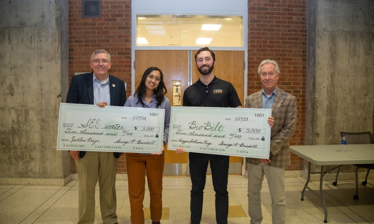Four people pose holding two oversized checks