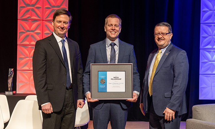 Ryan Sherman posing with a framed award alongside two other men