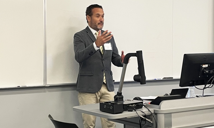 A man in a blazer speaks in front of a white board