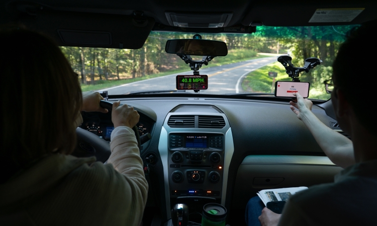 Two people in a car with smartphones mounted to the windshield driving on a road