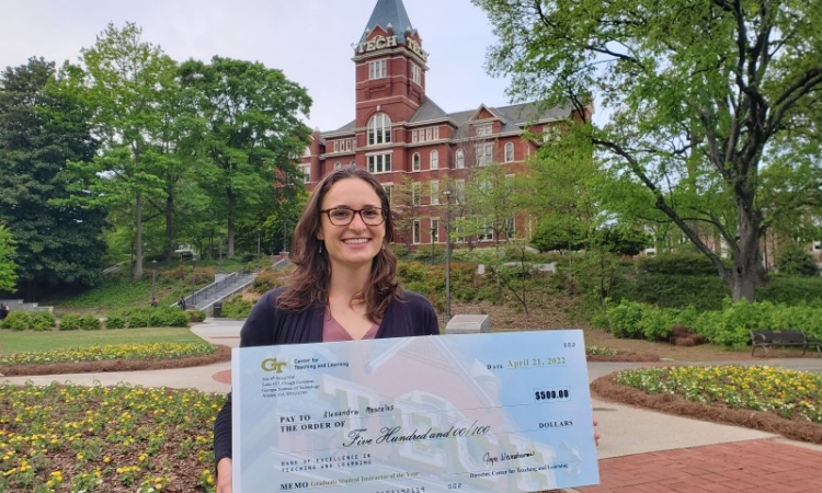 A woman holds a large check in front of a building 