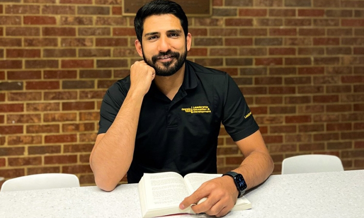 A man sits at a table with a book in front of a brick wall