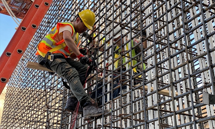 A man in a yellow hard hat and orange reflective vest works on a concrete sensor installation