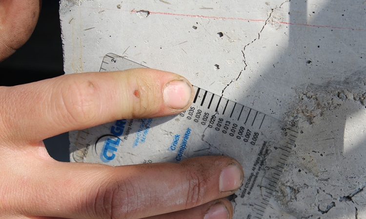 A researcher measures the width of a crack in a reinforced concrete column after testing the strength of the column. A new project funded by the U.S. Department of Energy Advanced Research Projects Agency will develop a field-deployable tool to detect cracks far smaller than this — and inside rather than outside — thick reinforced concrete structures. (Photo: Chris Kiser)