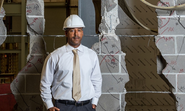 Reginald DesRoches stands with the ruptured cinder block wall one of his Ph.D. students destroyed while testing different kinds of masonry infill designed to strengthen similar structures in the Caribbean. DesRoches will draw on decades of earthquake research like this for the University of California, Davis, College of Engineering distinguished lecture he'll deliver in September. (Photo: Rob Felt)