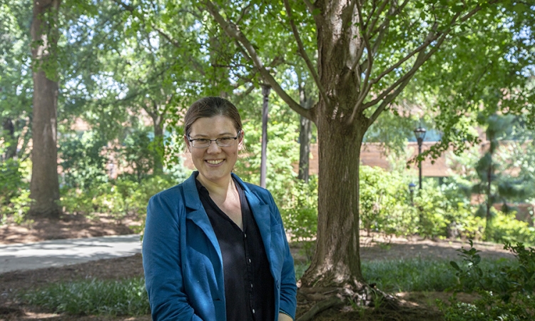 Emily Grubert is wearing a blue blazer and standing outdoors in front of a tree.