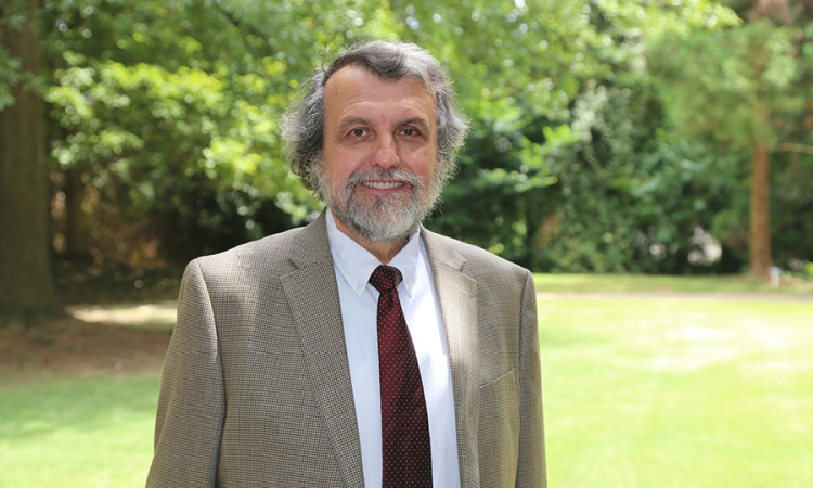 Michael Rodgers poses in a coat and tie with trees in the background