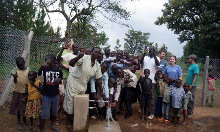 Oloo, Uganda, community members stand with the water pump that Engineers Without Borders has helped them construct.