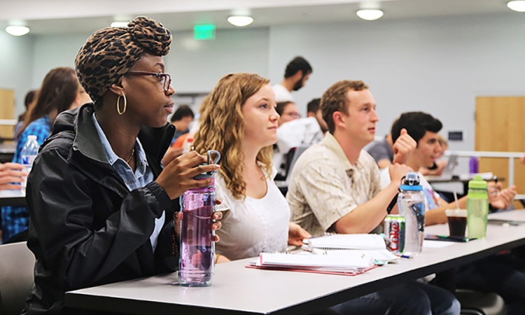 Four students sit attentitively at a long table in a lecture hall