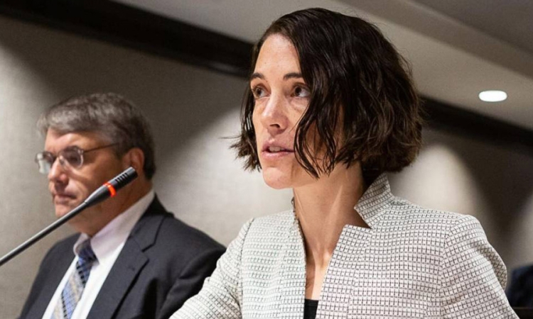 Gretchen Goldman wears a light blazer and sits before a microphone 