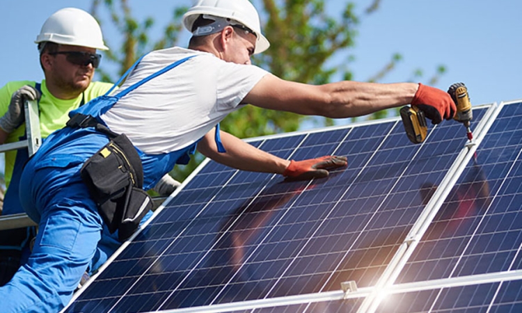 two men wearing white hard hats install solar panels 