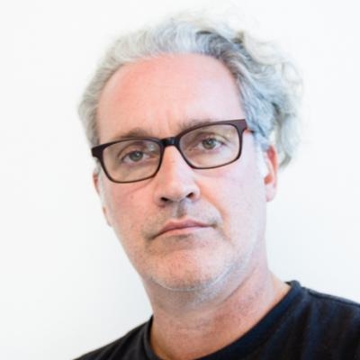 Grey haired man wearing brown glasses and a black t-shirt