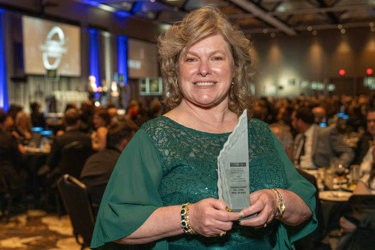 A woman in a green dress holds an award 