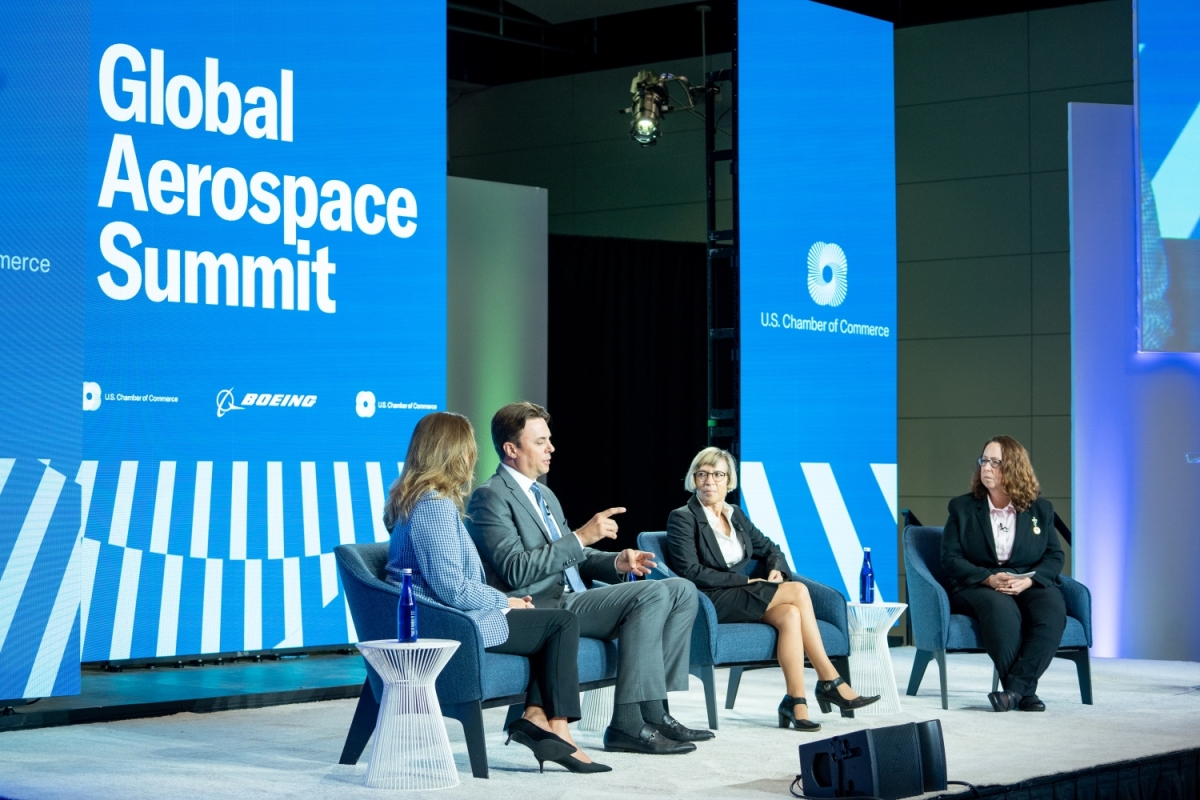 Four people sitting in chairs in front of a large sign that says Global Aerospace Summit