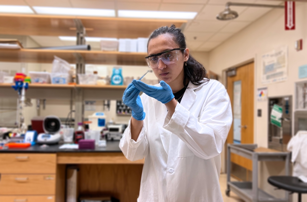 A woman wearing protective equipment holds a pipette in a laboratory