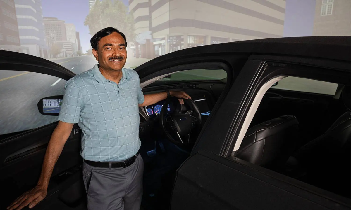 Srinivas Peeta stands with the car door open on the driving simulator in his lab.
