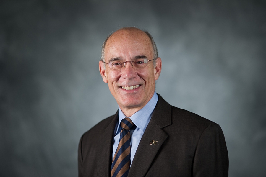 A man wearing a coat and tie smiles in a portrait 