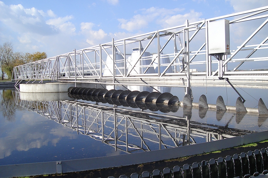 Biological wastewater treatment equipment reflected on smooth water with a blue sky and clouds.