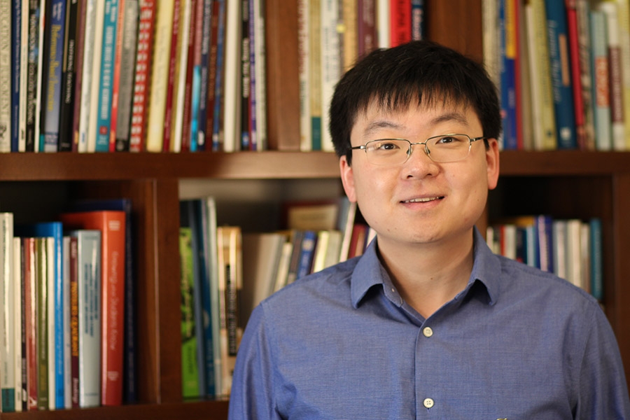 Ph.D. student Tuo Zhao stands in front of shelves filled with books. (Photo Courtesy: Center for Teaching and Learning)