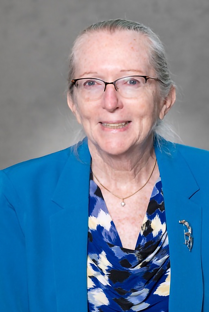 Portrait of Georgene Geary in a blue blazer with a silver brooch and a blue, black and white patterned blouse