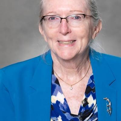 Portrait of Georgene Geary in a blue blazer with a silver brooch and a blue, black and white patterned blouse